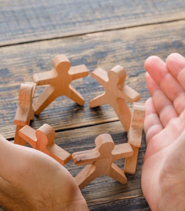 Business success concept on wooden background high angle view. hands protecting wooden figures of people.